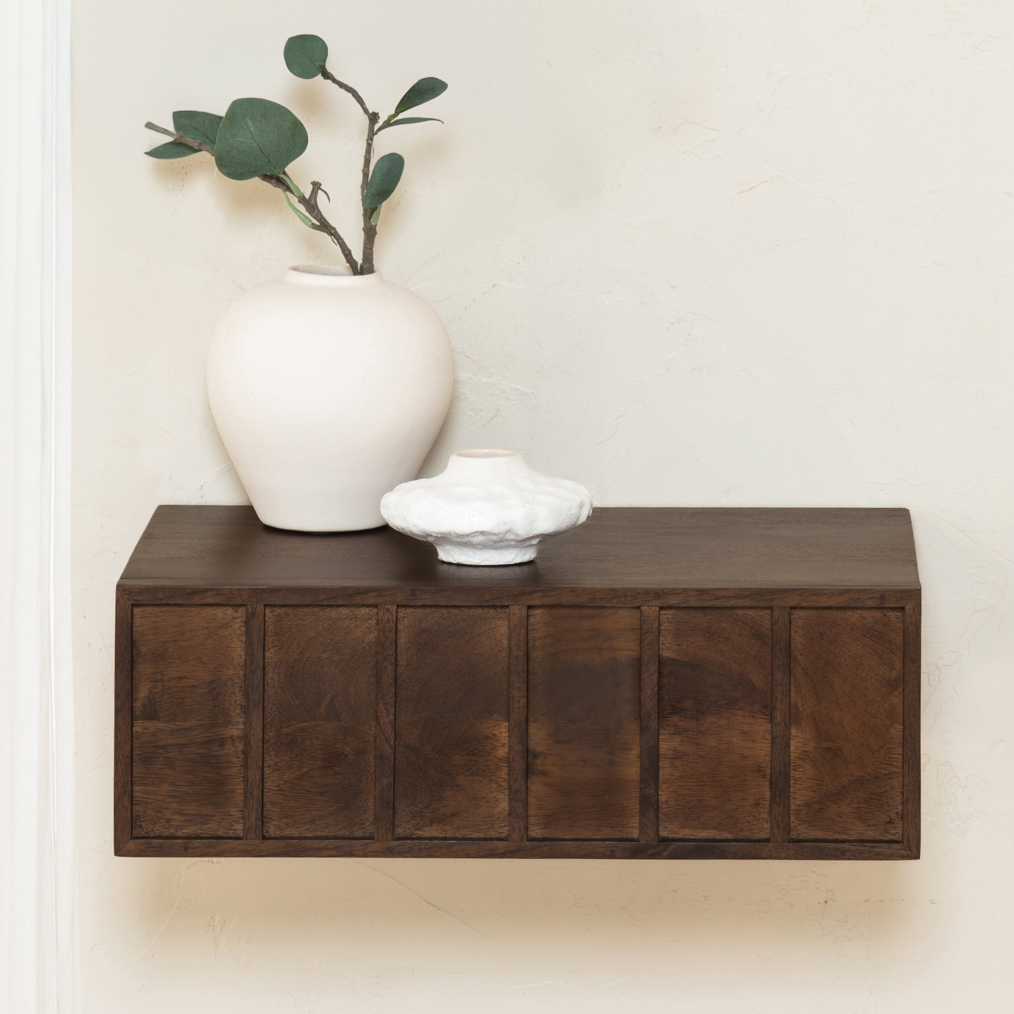 Wooden shelf with a white vase and plant against a plain wall