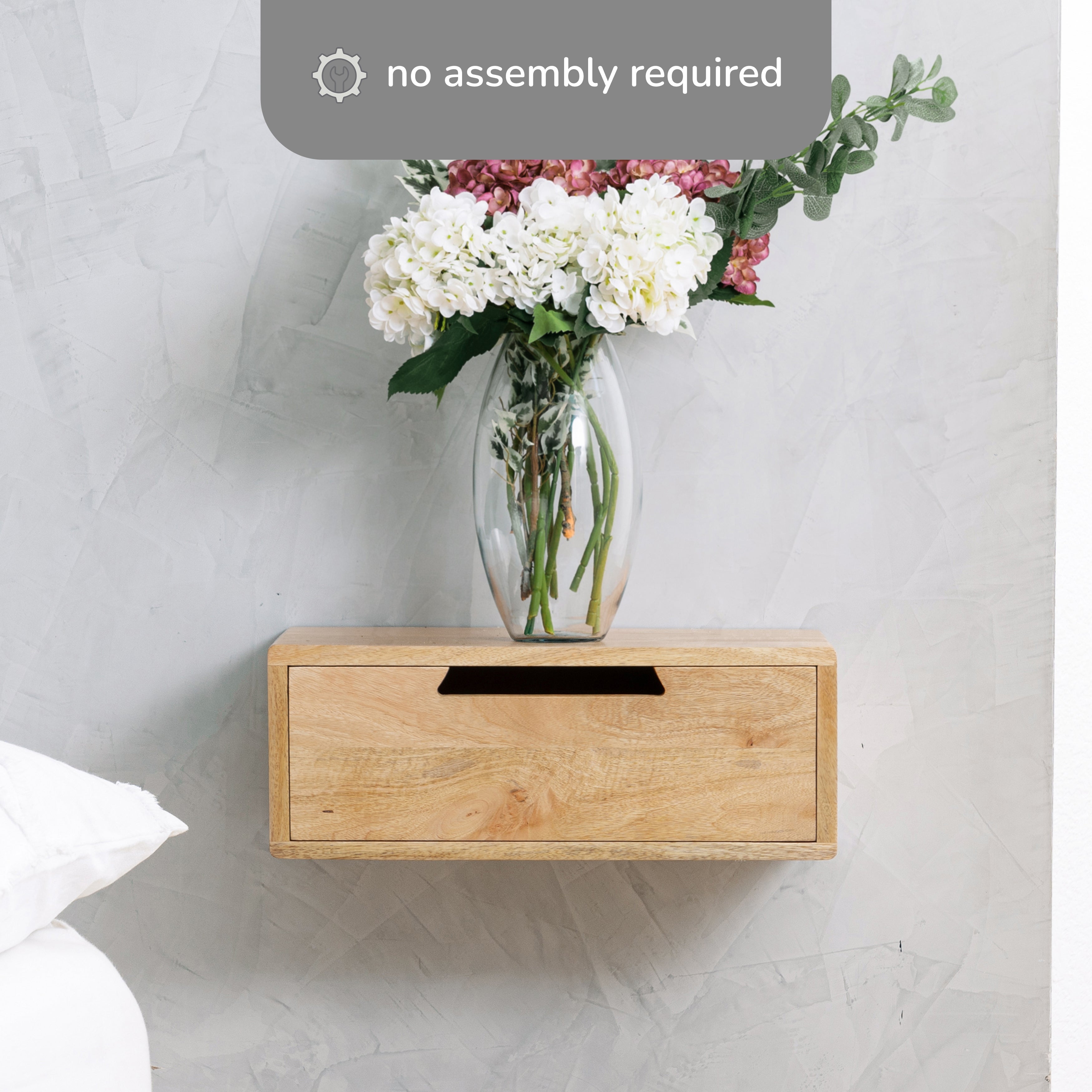 Wooden wall-mounted shelf with a clear vase of flowers on a light gray wall.