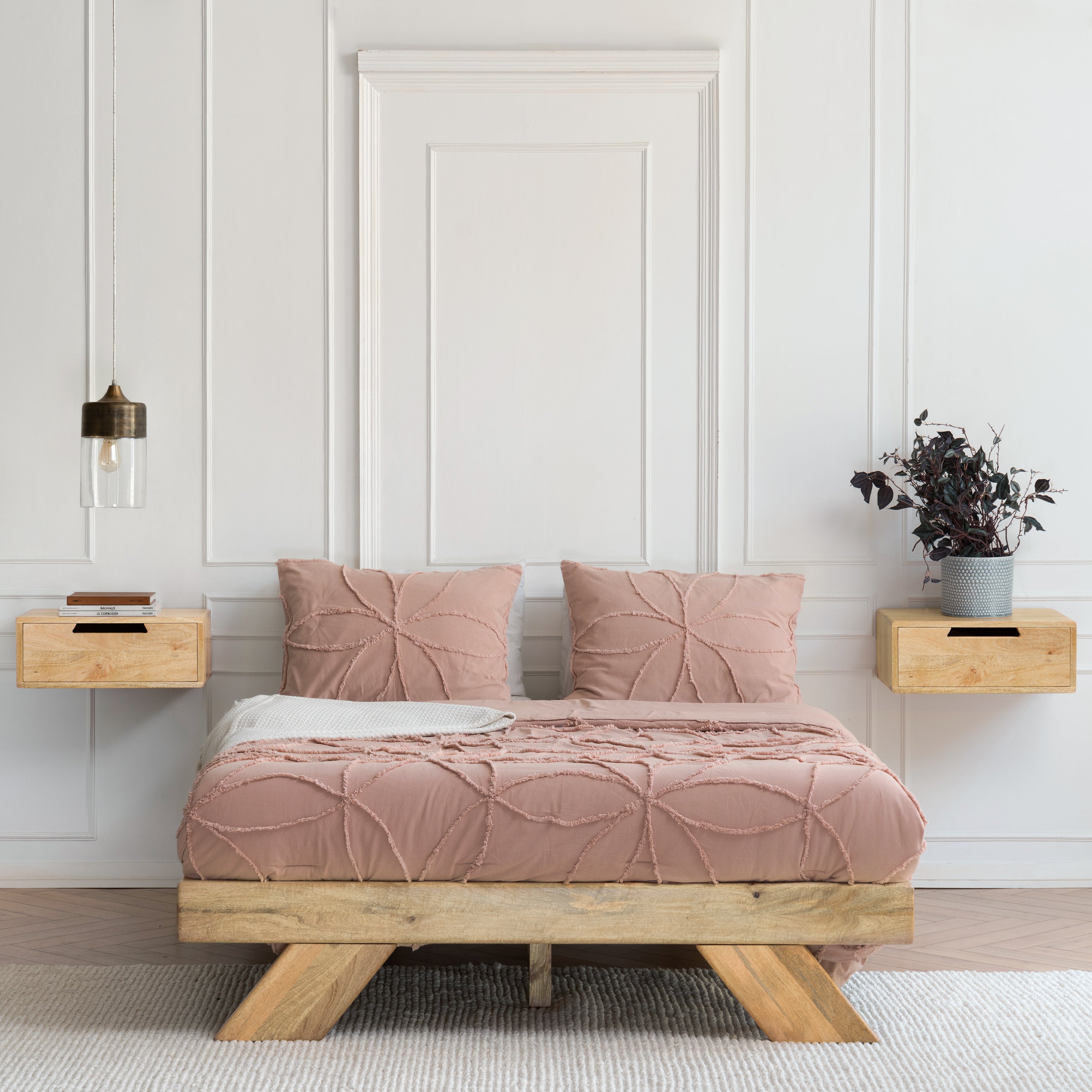 Bedroom with a wooden bed frame, pink bedding, and wall-mounted nightstands.