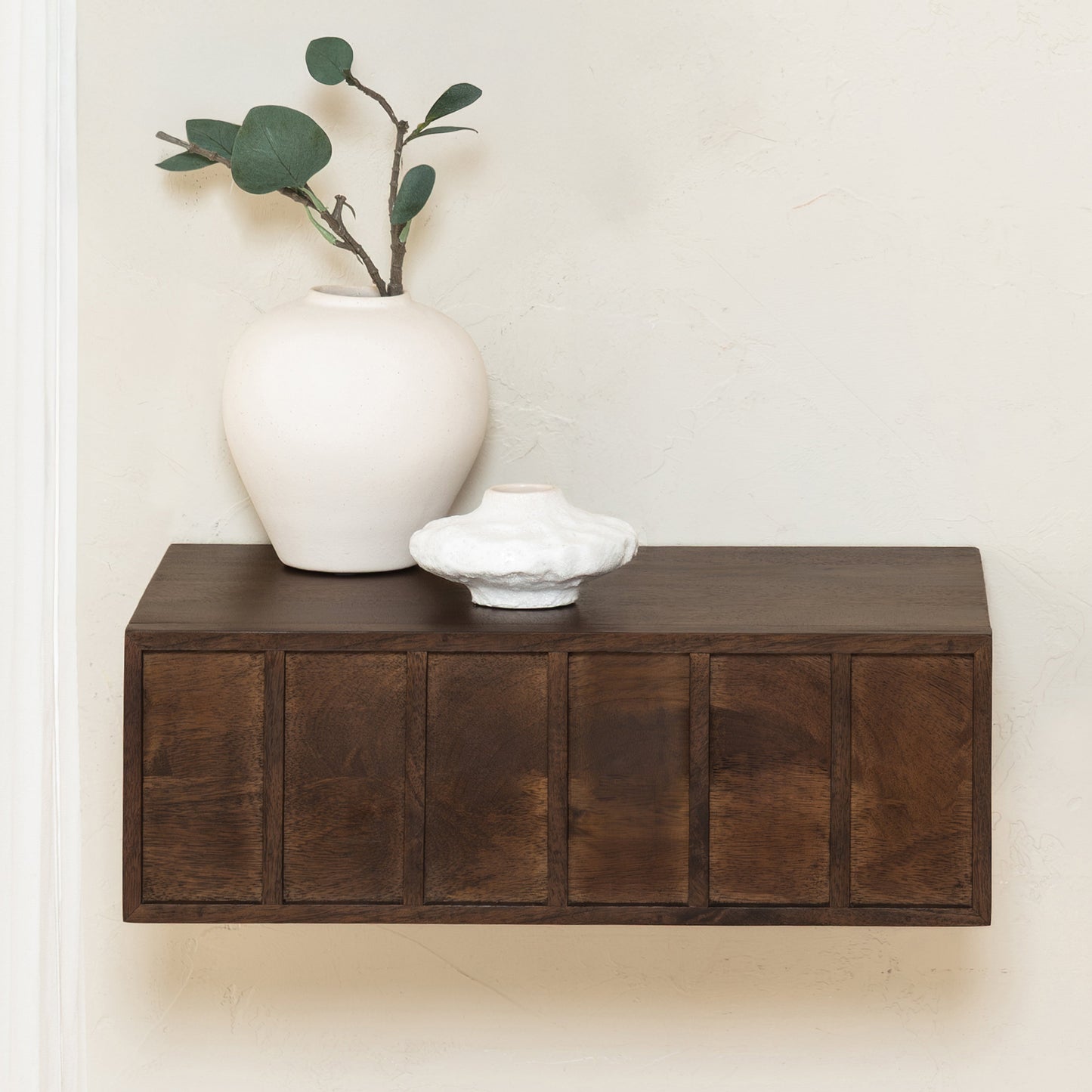 Wooden shelf with a white vase and plant against a plain wall