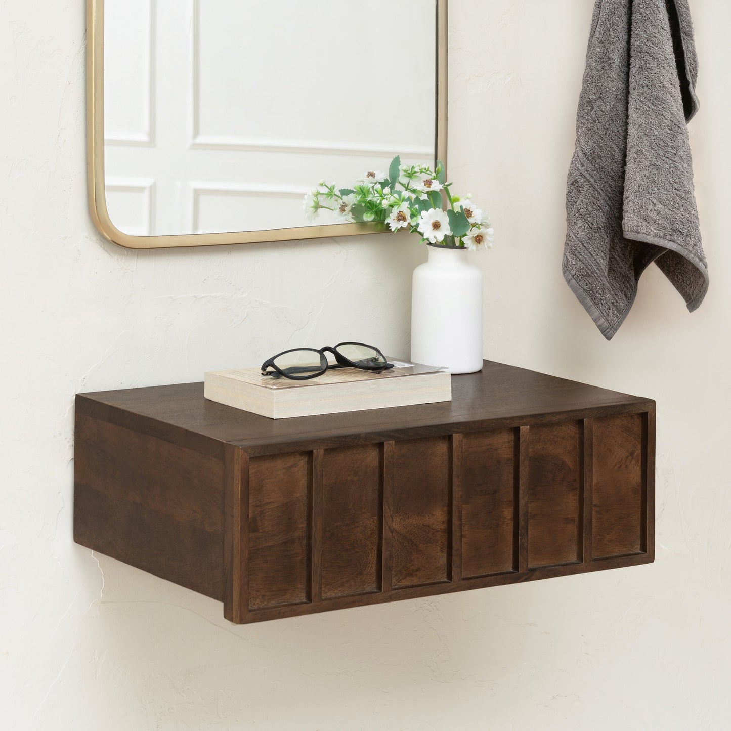 Wooden shelf with books, glasses, and a vase against a white wall.