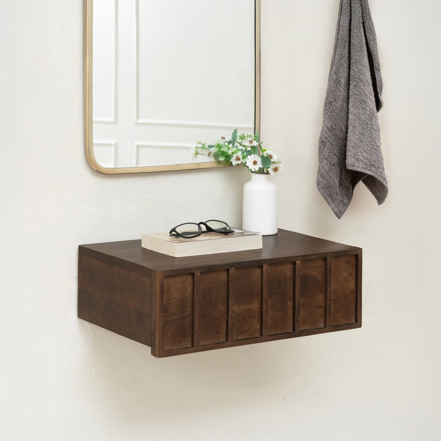 Wooden wall-mounted shelf with a mirror, books, and a vase on a white wall.
